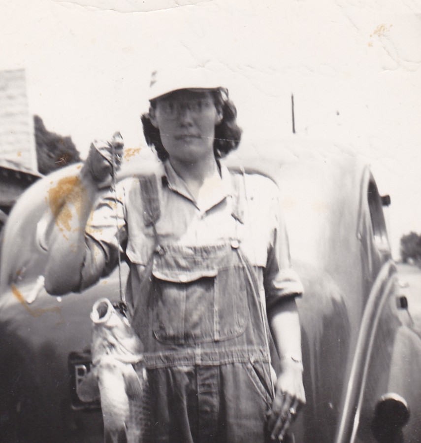 Mary Doan holding a large fish in front of an old car, June 1950